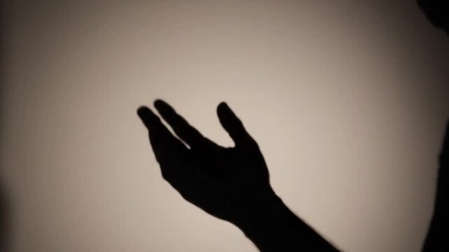 Silhouette of a human hand performing gestures against a plain background creating shadow art