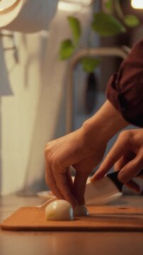 In a cozy kitchen, a man expertly slices a freshly peeled organic onion on a cutting board, releasing its pungent aroma into the evening air as he prepares a nutritious meal