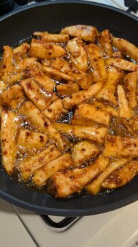 Sliced yellow plantain marinated with paprika and chilli spices fried on black cast iron pan, making patacones or kelewele