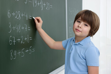 Schoolboy doing math on chalkboard in classroom