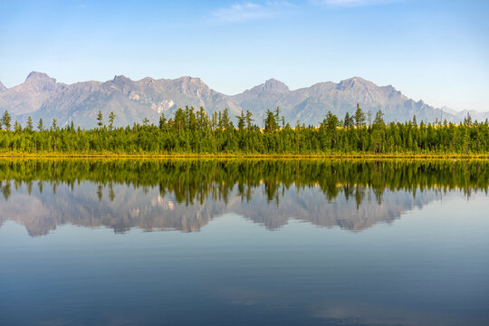 Serene mountain lake Tayozhnoye near Chara sands with clear reflection of Kodar mountain range and forest on water surface. Beautiful unspoiled nature landscape.