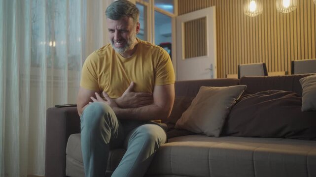 Medium shot of man hands massaging the stomach sits on couch feeling sudden strong abdominal ache, gastritis problem. Male having poisoning diarrhea indigestion peptic ulcer pancreatitis at home