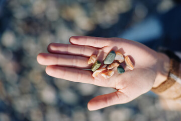 Hand holding colorful stones and pebbles in palm, outdoor nature setting, closeup detail and...