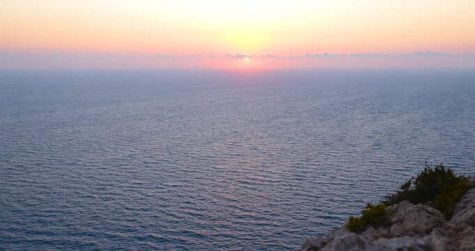 Sonnenaufgang &uuml;ber ruhiger Meeresfl&auml;che mit klarer Horizontlinie, erste Sonnenstrahlen steigen langsam aus dem Wasser auf, sanfte Farbverl&auml;ufe am Himmel und stille Morgenstimmung &uuml;ber dem Meer