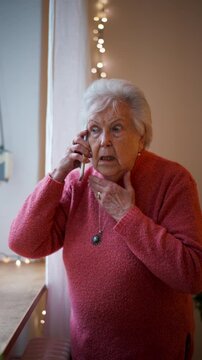 Old woman standing by window, making phone call.