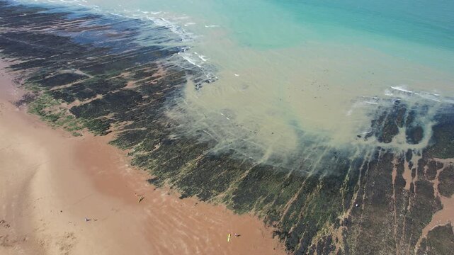 Drone Aerial view of coastline with sandy beach meeting the atlantic ocean. Waves create patterns over dark rocks and green algae. Margate botany beach Kent United Kingdom