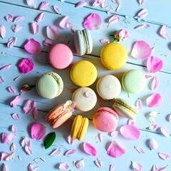 Top View of Pastel-Colored Macarons on Rustic Wooden Surface with Scattered Flower Petals, Romantic Dessert Concept
