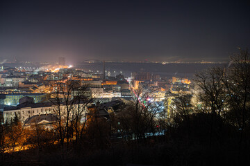 Naklejka premium Nighttime cityscape of Kiev, Ukraines Podil district Layered buildings with contrasting white and yellow lights, viewed from an elevated position The composition emphasizes depth and light contras