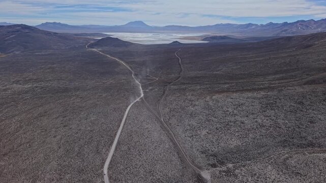 A high-altitude drone follows the final stretch of mountain road toward Laguna Salinas. Vast salt flats appear in the distance, framed by towering volcanoes surrounding the high Andean lagoon.