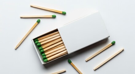 Obraz premium Open white matchbox filled with wooden matches and scattered green safety tips.