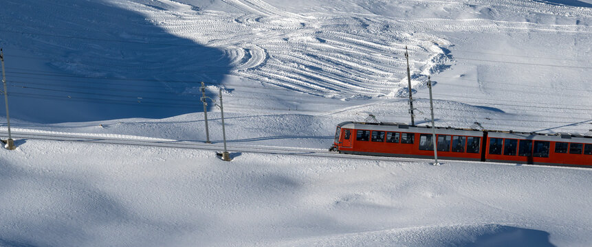 Orange Gornergrat Train Journeying Through Snowy Alpine Landscape Past Electrical Poles