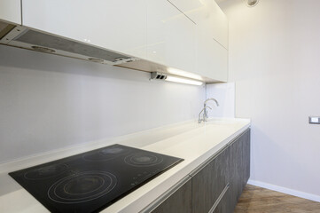 Modern kitchen with white countertop, black glass cooktop, stainless steel faucet, white cabinets, gray lower units, under-cabinet lighting, sleek design.