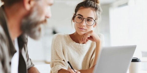 Focused woman with glasses listens intently during a work meeting at a modern office setting.