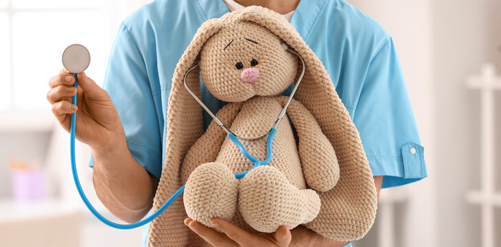 Male pediatrician with toy bunny and stethoscope in clinic, closeup