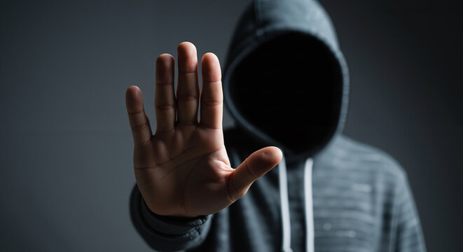 Anonymous person in a hoodie with stop hand gesture, a concept of anxiety, conflict, and refusal.