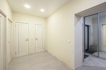 Light beige hallway with wooden-style flooring, three white doors, recessed ceiling lights, mirrored wardrobe, neutral walls, clean minimalist design.