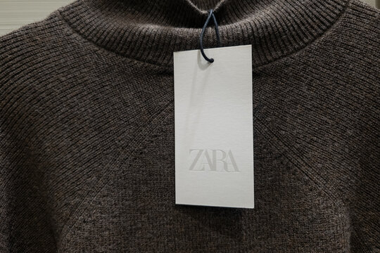 WARSAW, POLAND - JANUARY 21, 2026: A close-up view of a white price tag with the Zara brand logo attached to a brown ribbed knitted sweater