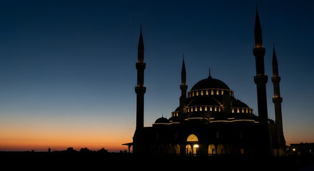 Naklejka premium Grand mosque illuminated at dusk, dark silhouette against twilight sky, warm lights glowing from within, majestic domes and minarets, peaceful evening scene, Islamic spiritual ambiance, architectural 