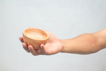 Hand holding empty small wooden bowl against a light background