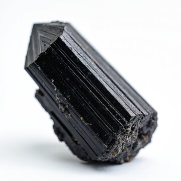 Black tourmaline mineral crystal isolated on white background. Natural prismatic schorl stone with rough base. Geometric mineral specimen macro view.