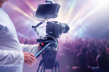 Video production operator films a live concert with a professional camera on tripod. Event...