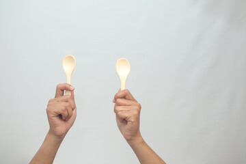Two Hands Holding Wooden Spoons Against White Background