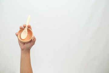 Hand holding empty wooden bowl with spoon against white background, ready for food preparation
