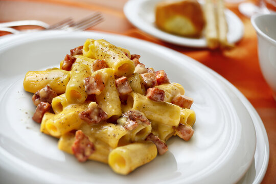 Plate with rigatoni carbonara pasta on a laid table