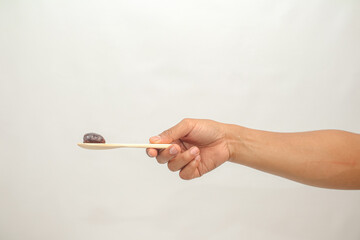 Hand holding wooden spoon with small dark berry or raisin against white background