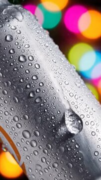 Macro shot of cold aluminum can surface covered in condensation, featuring glistening water droplets and a dramatic, abstract background of multicolored neon bokeh lights, symbolizing refreshment