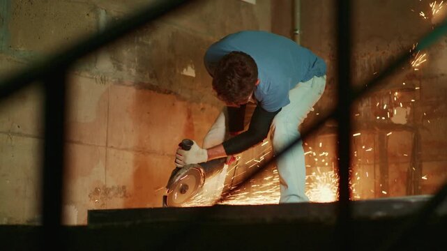 worker cutting metal seen through railing, angled viewpoint reveals sparks and concentrated motion, protective clothing and gritty basement atmosphere, renovation at dusk