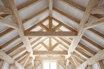 Wooden roof truss construction with natural timber beams and white ceiling panels creating bright and spacious interior with visible structural framework and craftsmanship
