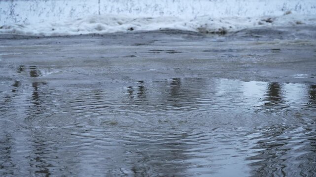 Slushy winter street with melting dirty snow and puddles on rainy day. Raindrops fall on puddles