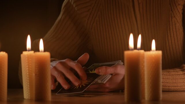 Male fortune teller reading tarot cards by candlelight in darkness