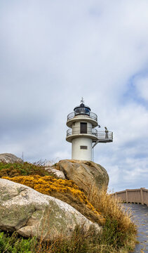 White lighthouse on rocky cliff under cloudy sky