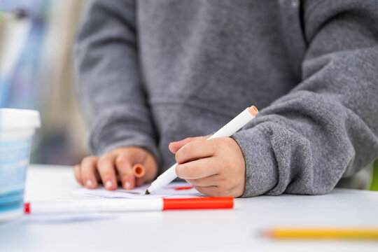 A young student writes or draws with a marker during an art class at school or summer camp. The little girl grips the red marker tightly in her small fist. 