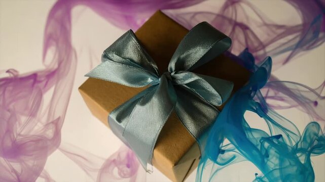 A brown gift box with a teal bow against a backdrop of swirling purplish-blue smoke