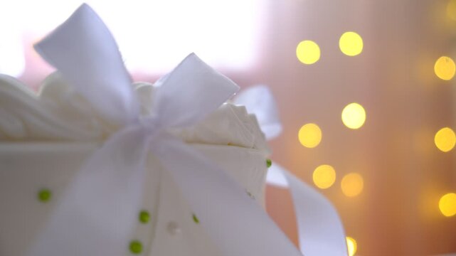 Wedding cake with white cream cheese, cake tier.  Cake decorated white bows. Festive background with string lights. Soft blurred, cinematic mood