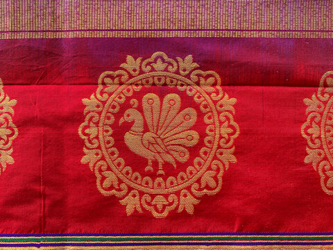 A close-up of a traditional Indian silk saree fabric showcasing a prominent circular peacock motif intricately woven in rich golden zari.