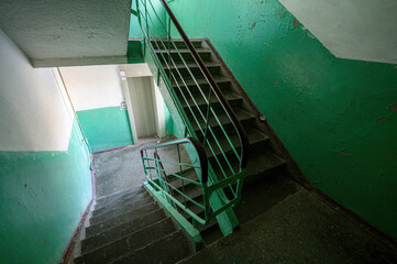 Narrow staircase in residential building with green-painted walls, metal railings, worn concrete steps, dim lighting  utilitarian, aged communal space. © evgeniykleymenov