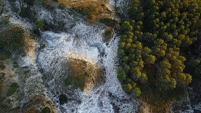 An aerial shot filmed with a drone shows a natural landscape from above. The camera moves smoothly over uneven, rocky terrain. Scattered trees and mountainous terrain appear.