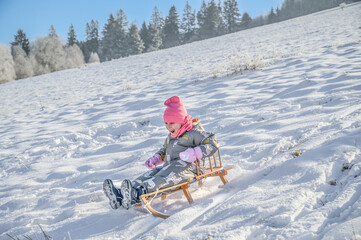 A joyful child sledging on a wooden sledge, surrounded by a picturesque winter landscape, showing pure delight while enjoying the snow on a bright sunny day.