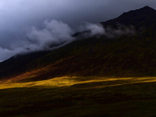 Golden sunlight illuminates a distinct path across the lower slopes of hill in Ireland.
