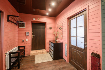 Fototapeta premium Cozy hallway with pink wooden paneling, dark wood doors, built-in storage unit, radiator, shoe rack, frosted glass door, decorative wall elements, woven rug.