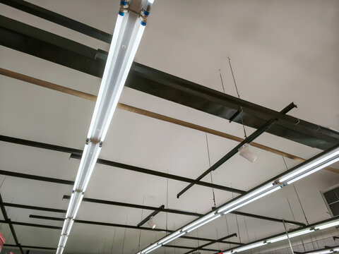 Low angle shot of bright LED tube lights installed on a white industrial ceiling with black metal frames. A professional lighting setup for modern warehouses, retail stores, and commercial offices.