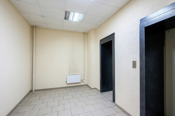 Fototapeta premium Narrow office hallway with tiled floor, beige walls, ceiling fluorescent lights, electric heater, two doorways, plain minimalist design, clean and uncluttered.