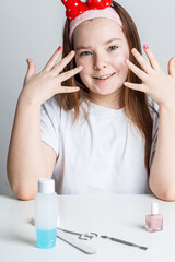 Fototapeta premium A little teenage girl shows off her first manicure while sitting at a white table at home.