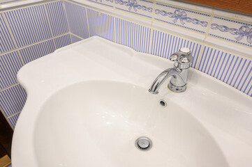 Fototapeta premium White ceramic bathroom sink with chrome faucet, set against blue-striped tiled wall with decorative floral border tiles. Clean, classic design, functional layout.