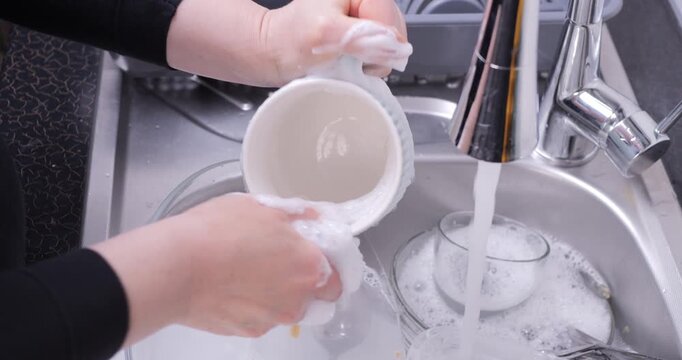 Close-up of a hand washing a mug in a sink full of dishes with soap and water. Dish washing, kitchen cleaning and household hygiene concept.