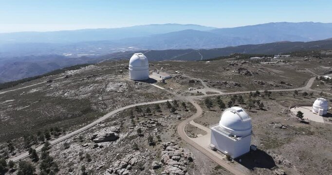 Drone establishing shot of Calar Alto Observatory domes on rocky plateau with distant mountains in Spain astronomy research landscape